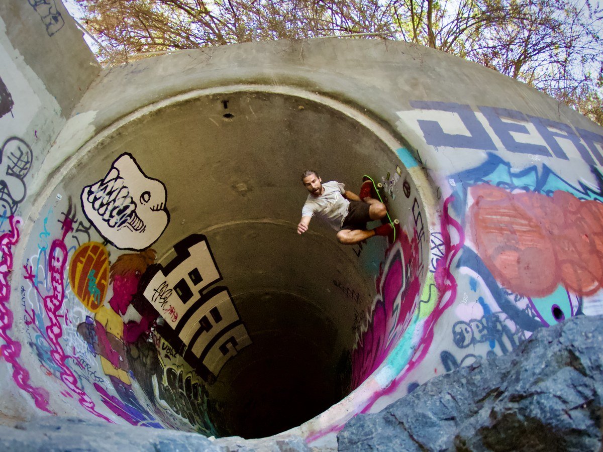 Skater carving high on the vertical wall of a graffiti-covered concrete pipe
